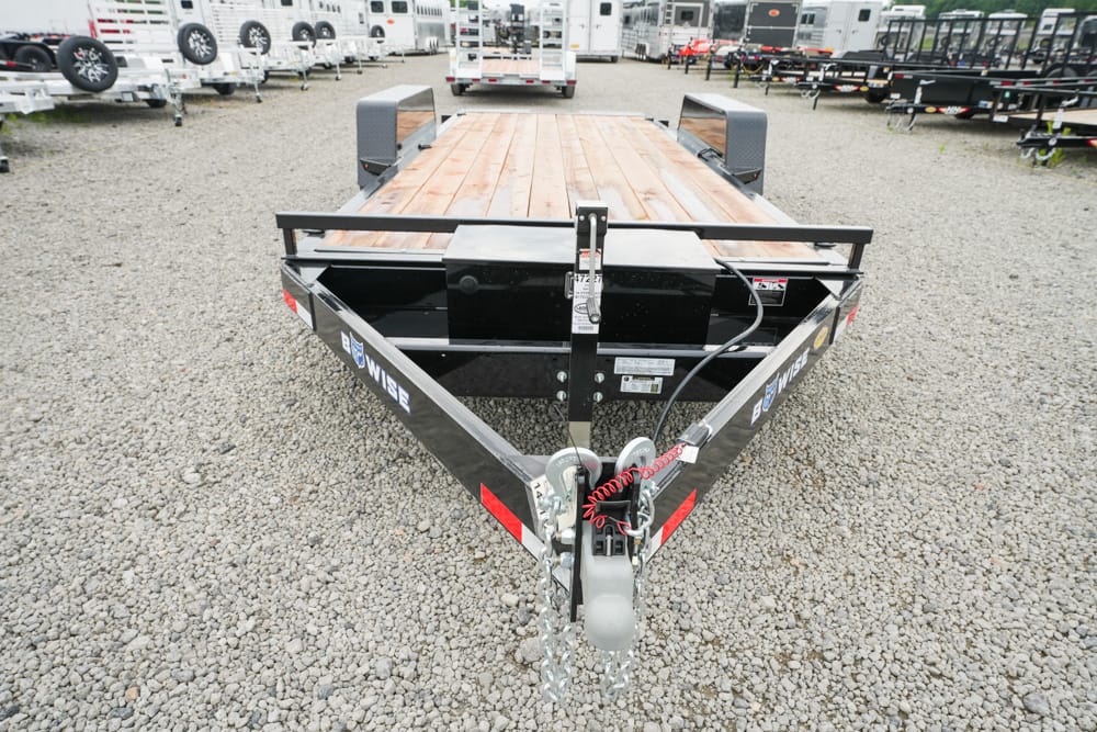 Front view of a black open utility trailer on a gravel lot, wood deck and safety chains at the hitch.