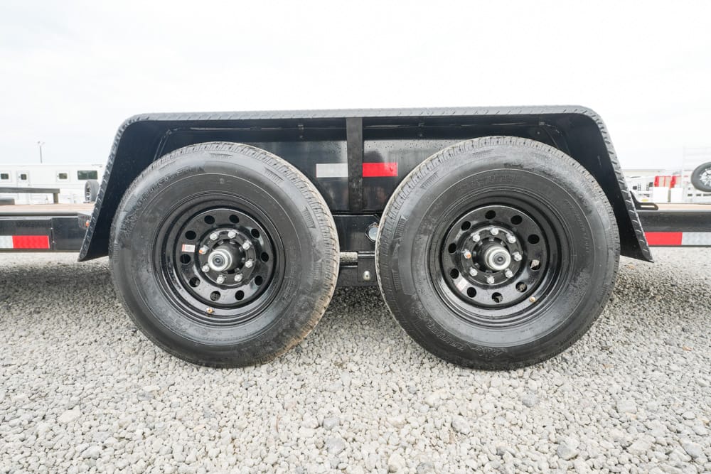 Dual wheels of a heavy-duty trailer with black rims under a rounded fender on a gravel surface