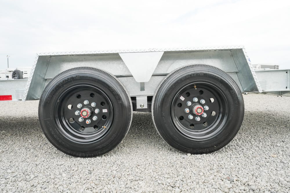Dual-axle trailer with black steel wheels and a metal fender on a gravel lot,”,