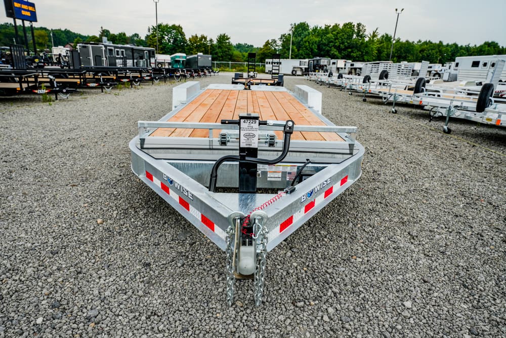 Front-facing utility trailer with a wooden deck in a gravel trailer yard, with many trailers in the background