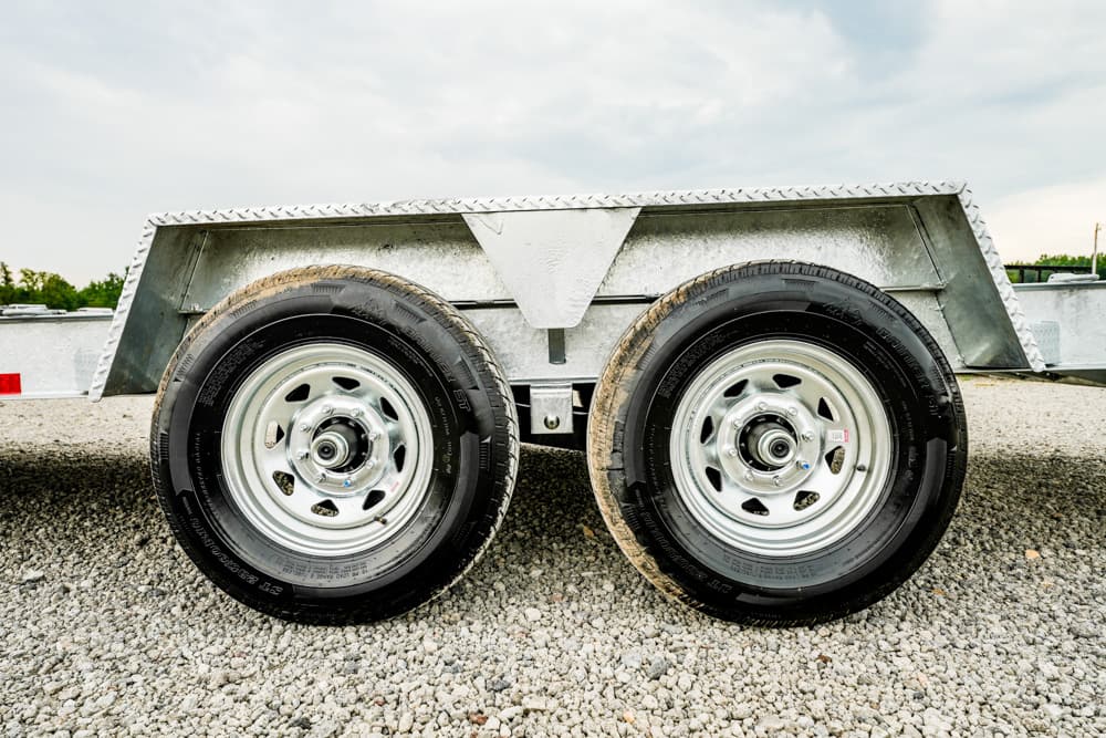 Dual-axle trailer wheels with a metal fender on a gravel surface, close-up view