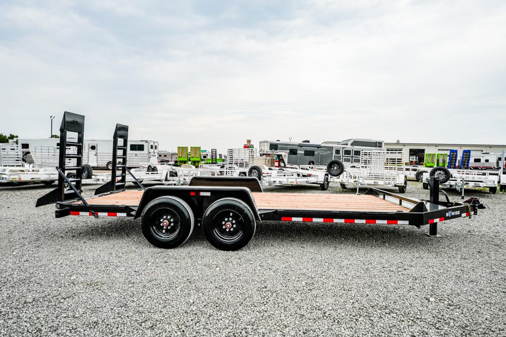 Black dual-axle flatbed trailer with ramps on a gravel trailer yard