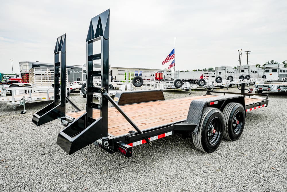 Black steel car hauler trailer with wooden deck and dual loading ramps in a gravel lot