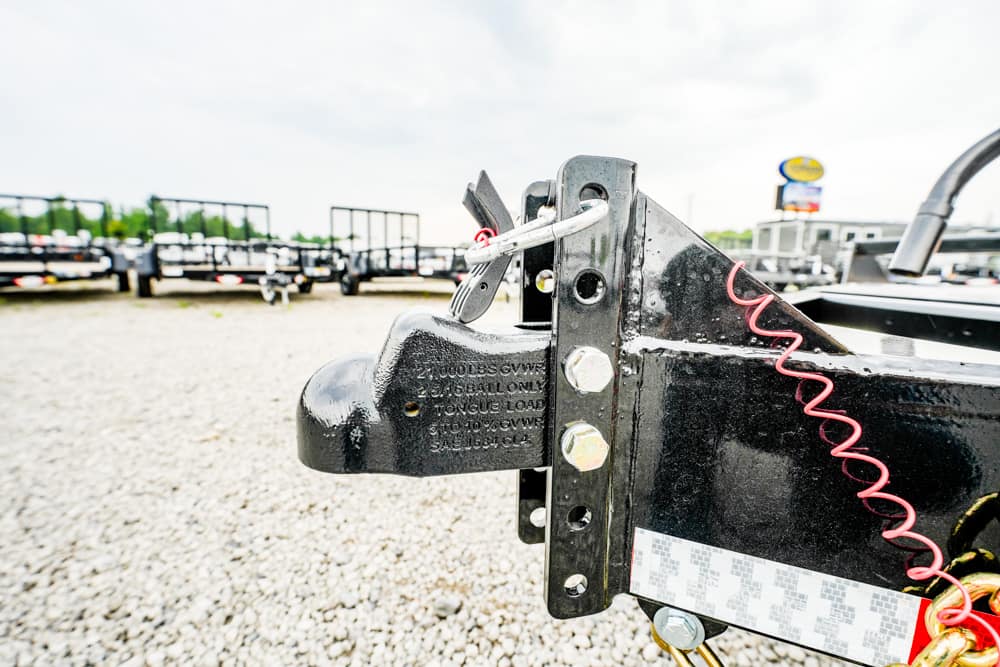 Close-up of a black trailer hitch and coupler with a red coiled safety cord on a gravel lot.
