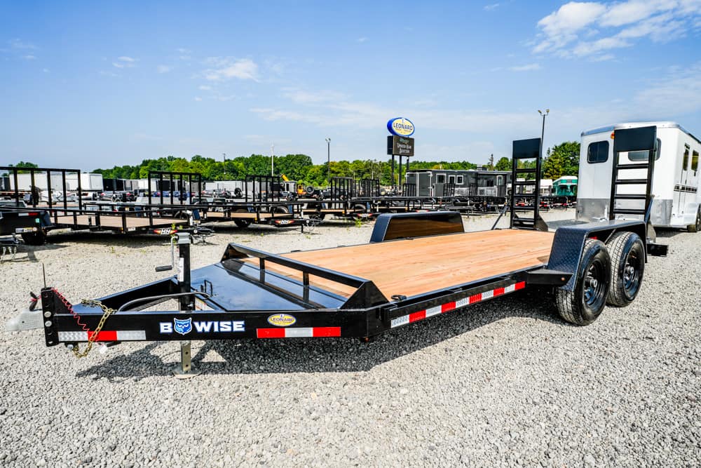 Flatbed car trailer with a wooden deck in a gravel trailer lot, ready for transport services, with other trailers in the background.