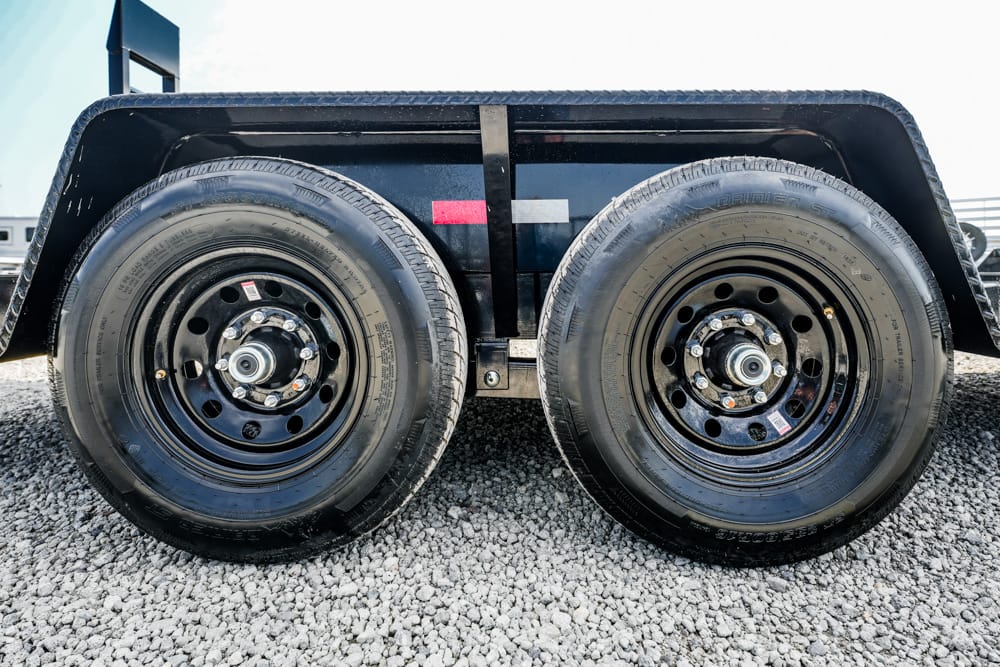 Dual trailer wheels with black rims on a gravel surface, under a black fender edge