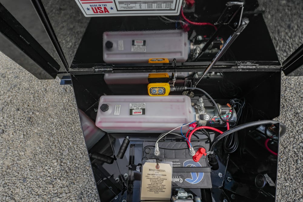 Open equipment battery bay with a 12V battery, red/black cables, and a yellow diagnostic device inside a black metal chassis.