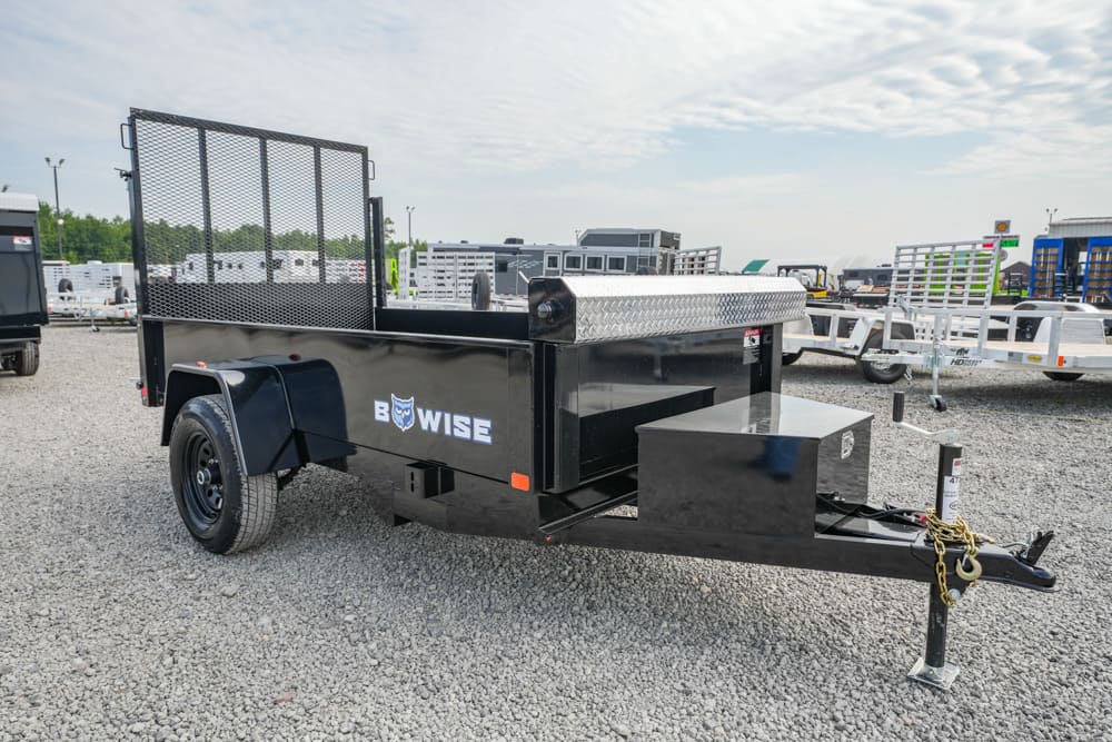Black utility trailer with a diamond-plate toolbox and mesh ramp gate, on a gravel lot with other trailers in the background—logo reads 'BOWISE' on the side, ready to haul equipment.