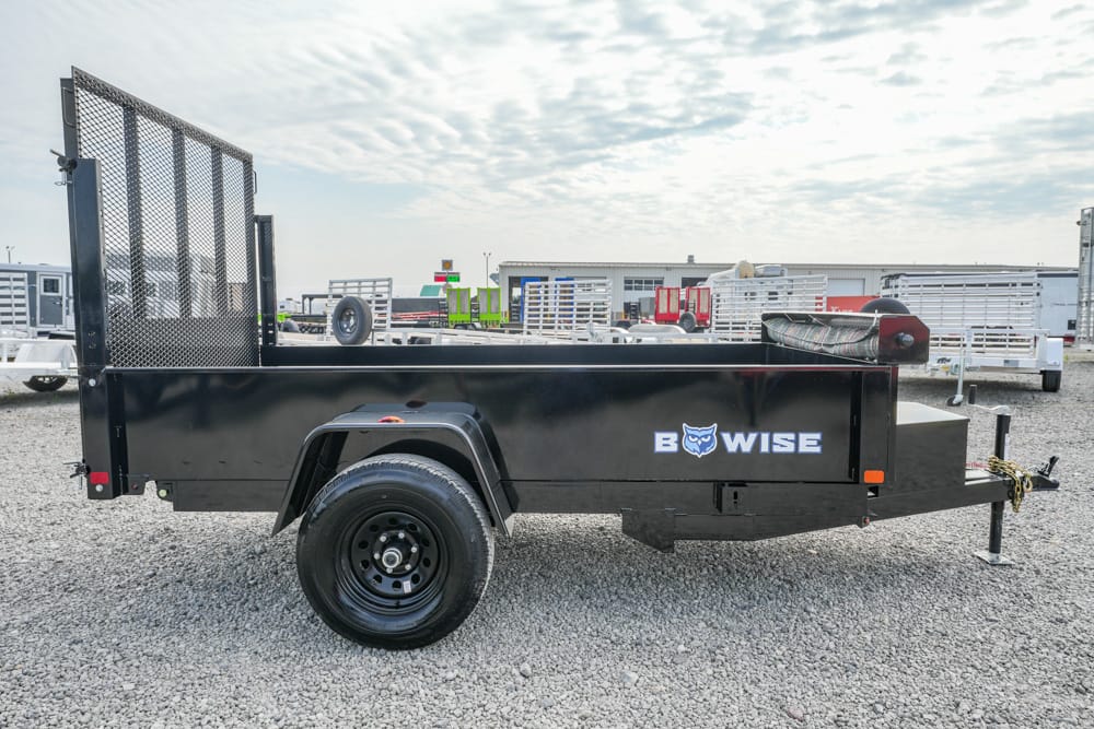 Black B‑WISE utility trailer shown in a side profile with a tall mesh rear ramp on a gravel lot