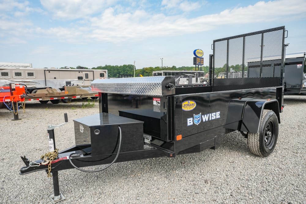 Black utility trailer with diamond-plate toolbox and rear mesh ramp, branded BowWise, on a gravel lot.