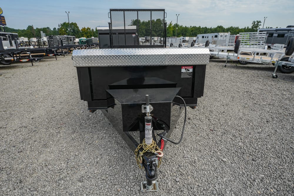 Utility dump trailer on a gravel lot, black with a diamond-plate top and a front hitch with safety chains visible in the foreground.
