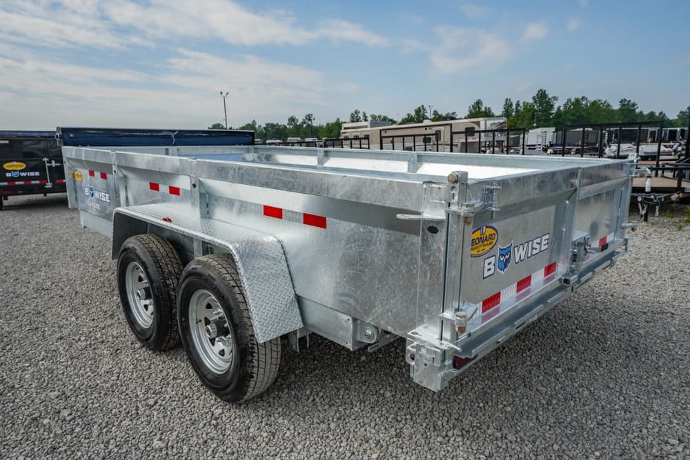 Silver dual-axle open-top utility trailer on a gravel lot with red reflective strips and diamond-plate fenders.