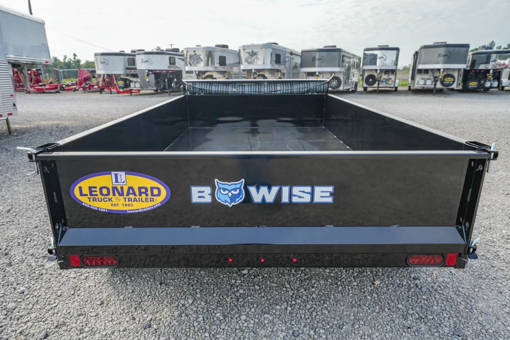 Back view of a black BowWise dumping trailer with a Leonard Truck & Trailer logo, parked among other trailers on a gravel lot.