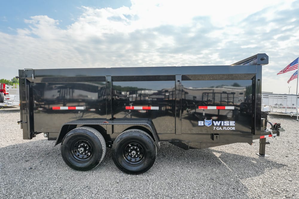 Black tandem-axle dump trailer with red/white reflective stripes on a gravel lot