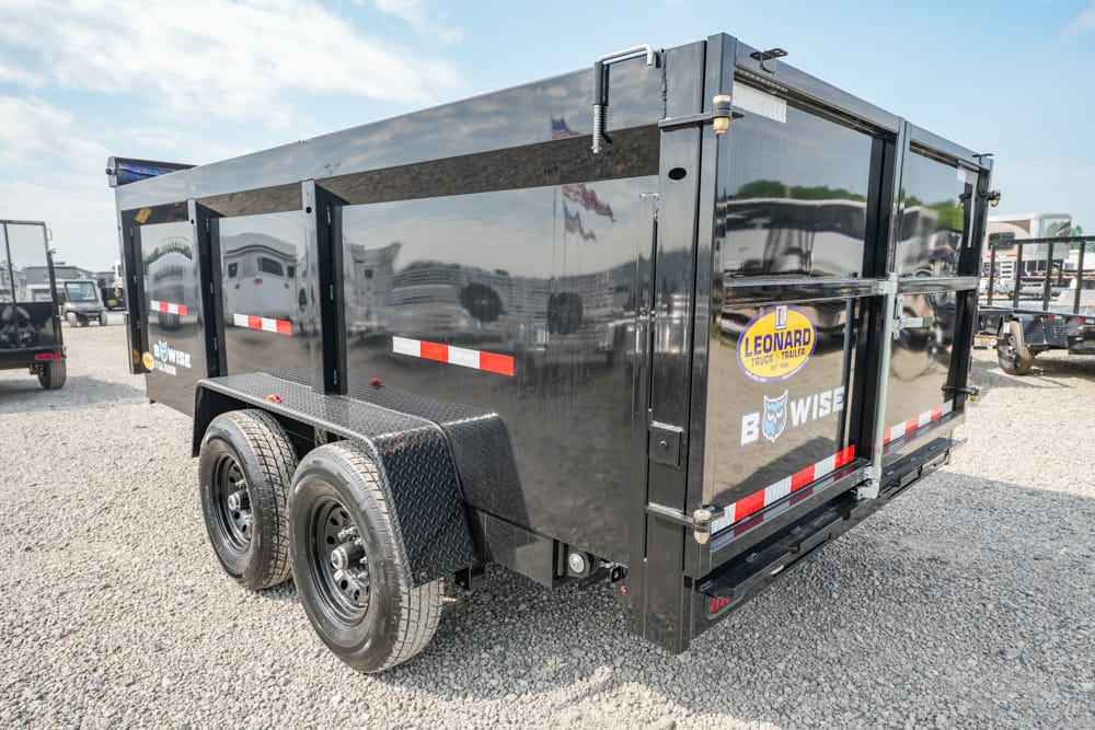 Black tandem-axle dump trailer in a gravel lot, with diamond-plate fenders and red/white reflective stripes