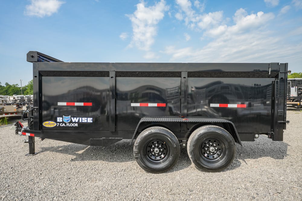 Black dump trailer with tandem wheels on a gravel lot, side logos and red/white reflective stripes along the container.