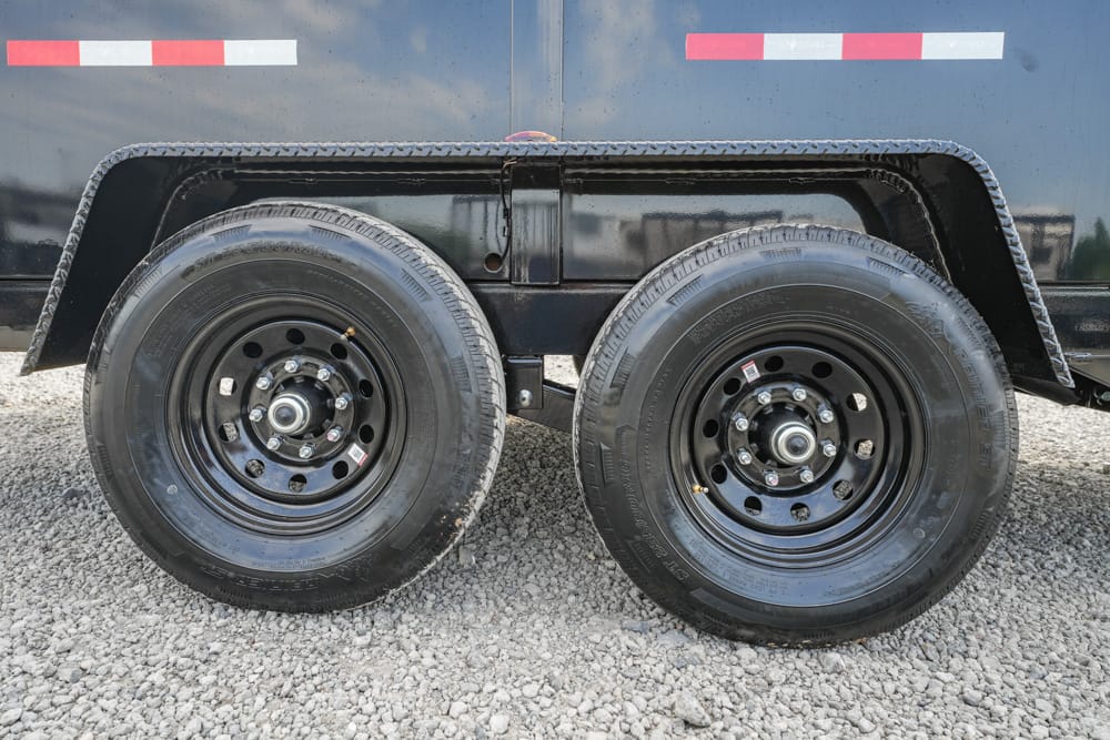 Dual-axle trailer with two black steel wheels on a gravel surface; undercarriage and fender visible, blue trailer side with red/white reflective strips.