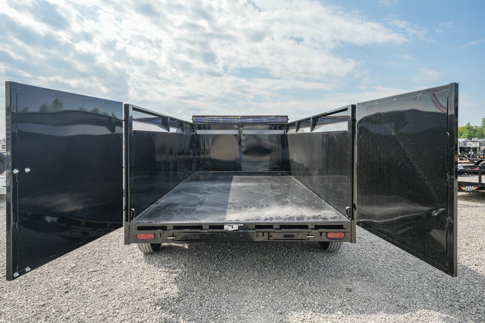 Empty black dump trailer with rear doors open, showing metal floor and side walls on a gravel lot.