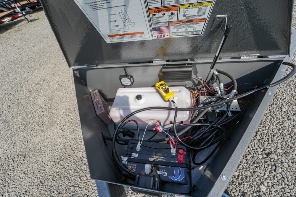 Open service panel with a car battery, white reservoir, and a tangle of wires; a yellow handheld meter rests on top.