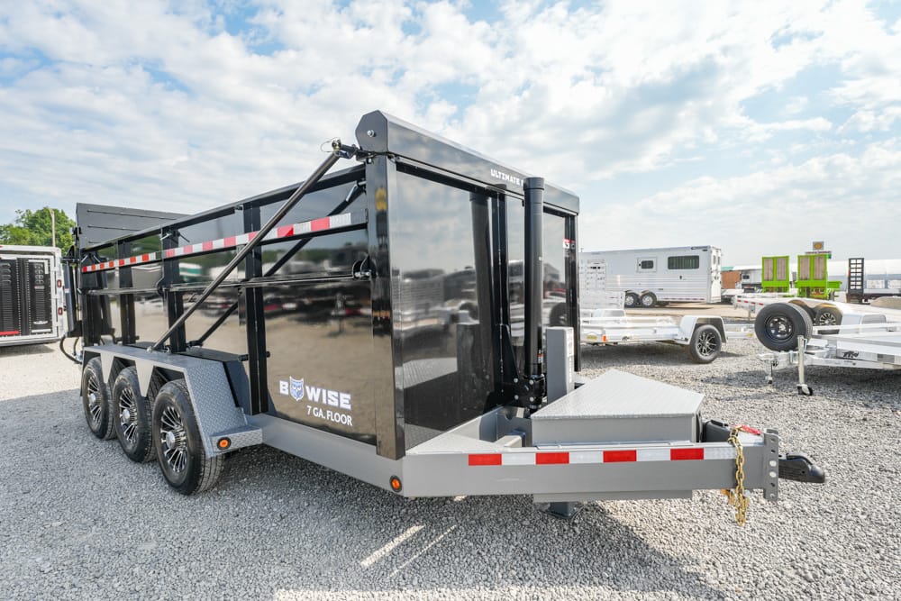 Black Bowise 7 GA Floor dump trailer with three axles, parked on a gravel lot with other trailers nearby.