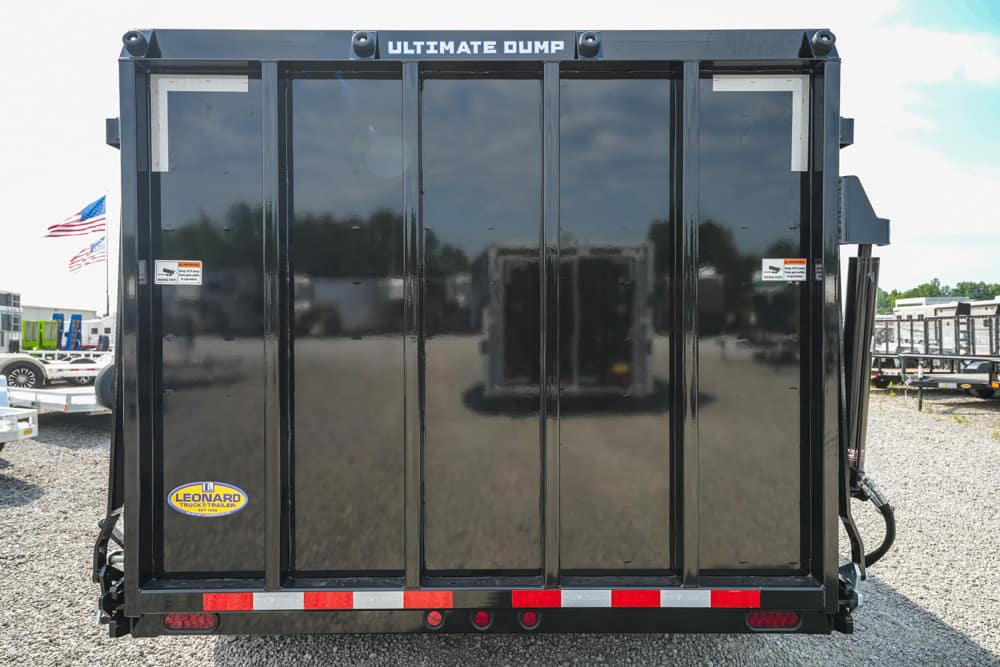 Back view of a black dump trailer labeled 'Ultimate Dump' with red reflectors and a Leonard trailer sticker.