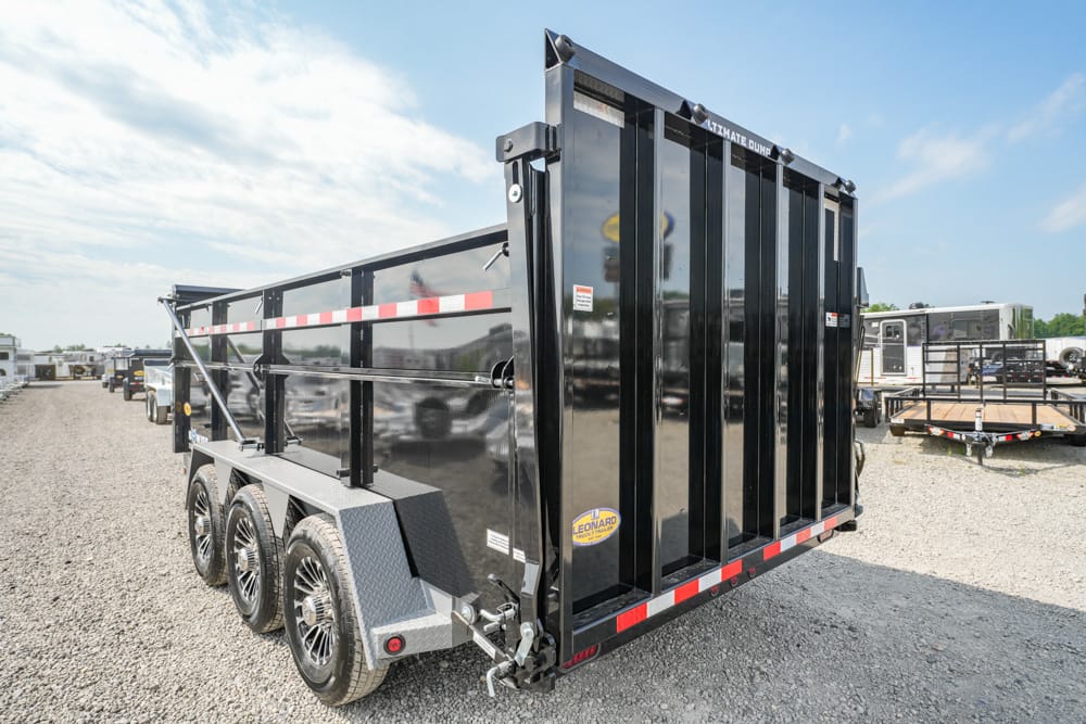 Black multi-axle dump trailer parked on a gravel lot, with red/white reflective side markings and tall rear gate.