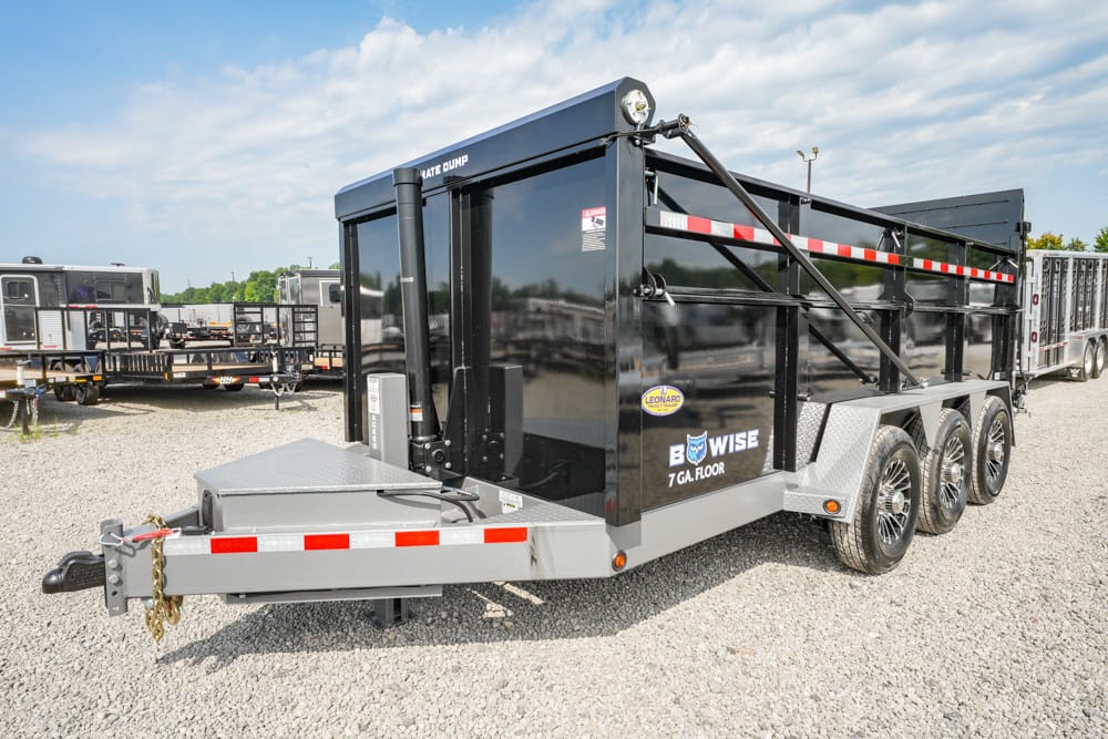 Black three-axle dump trailer with a diamond-plate front hitch on a gravel lot; labeled “B Wise” and “7 GA FLOOR.”
