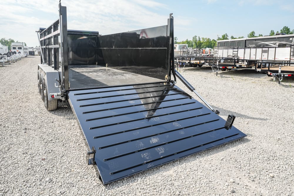 Black dump trailer with a lowered ramp gate on a gravel lot, with other trailers visible in the background.