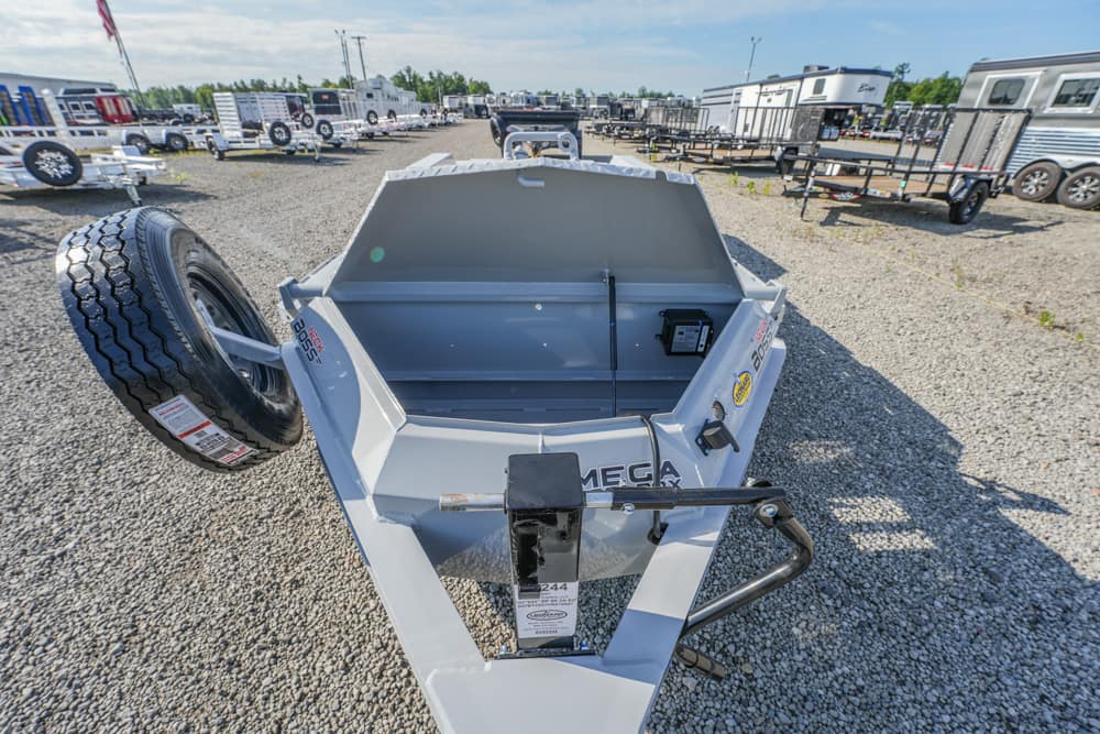 Gray dump trailer with an open bed and a spare tire mounted on the left, in a large lot of trailers.