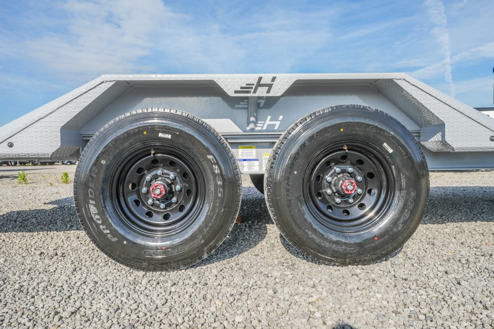Dual trailer wheels with black rims and red center caps on a gravel lot (tandem axle).