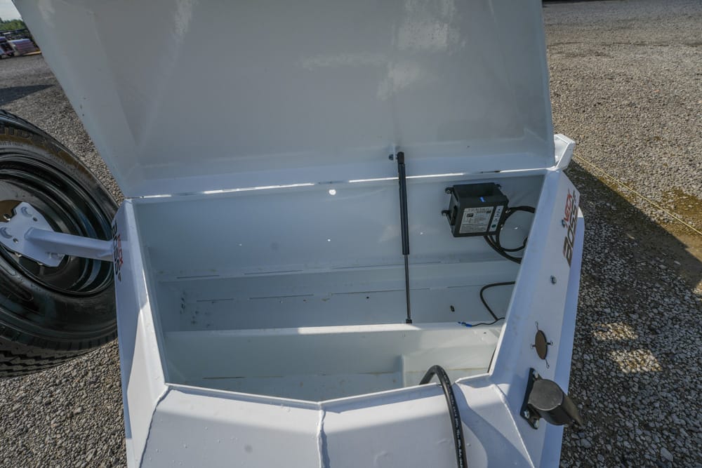Open white trailer storage box with lid raised, showing an empty interior, a vertical gas strut, and a mounted battery box with cables on the right side.