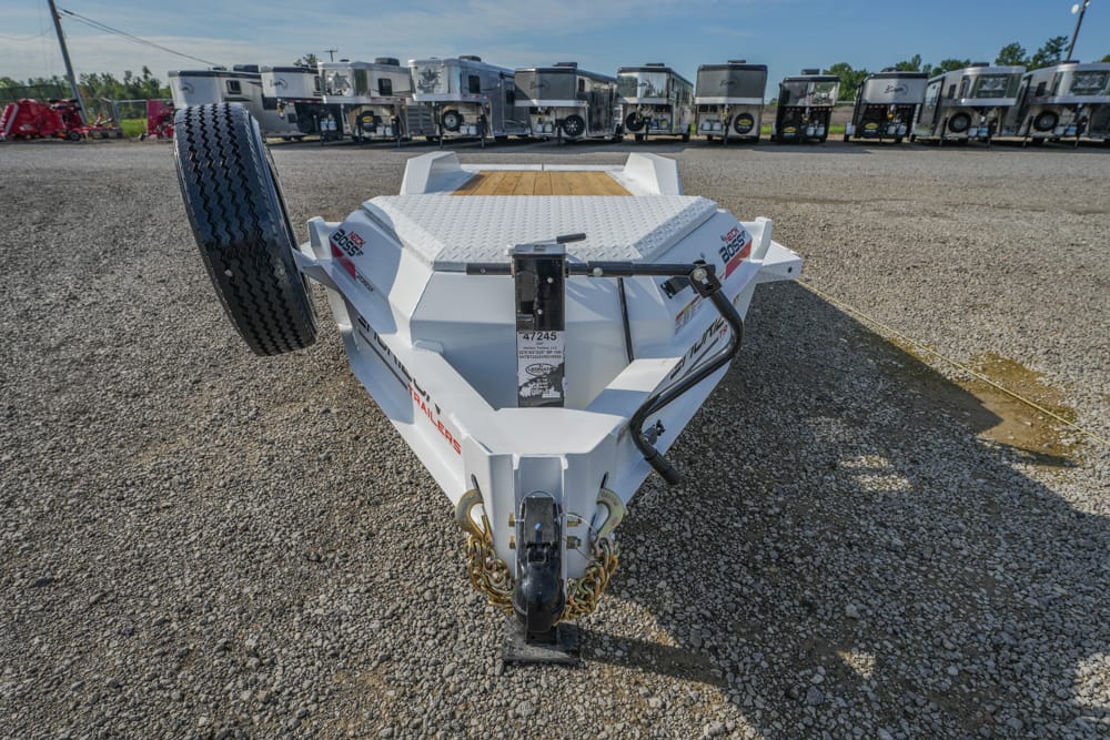 Front view of a white utility trailer on a gravel lot, spare tire on the left and many trailers in the background.