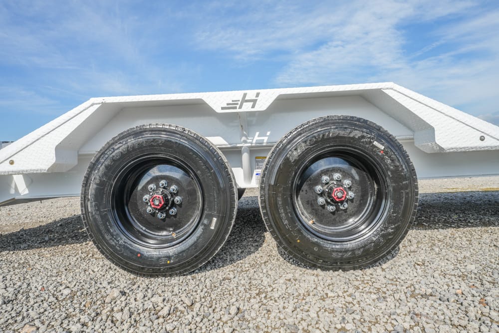 Dual-axle trailer with two black rims on a gravel surface under a clear blue sky.