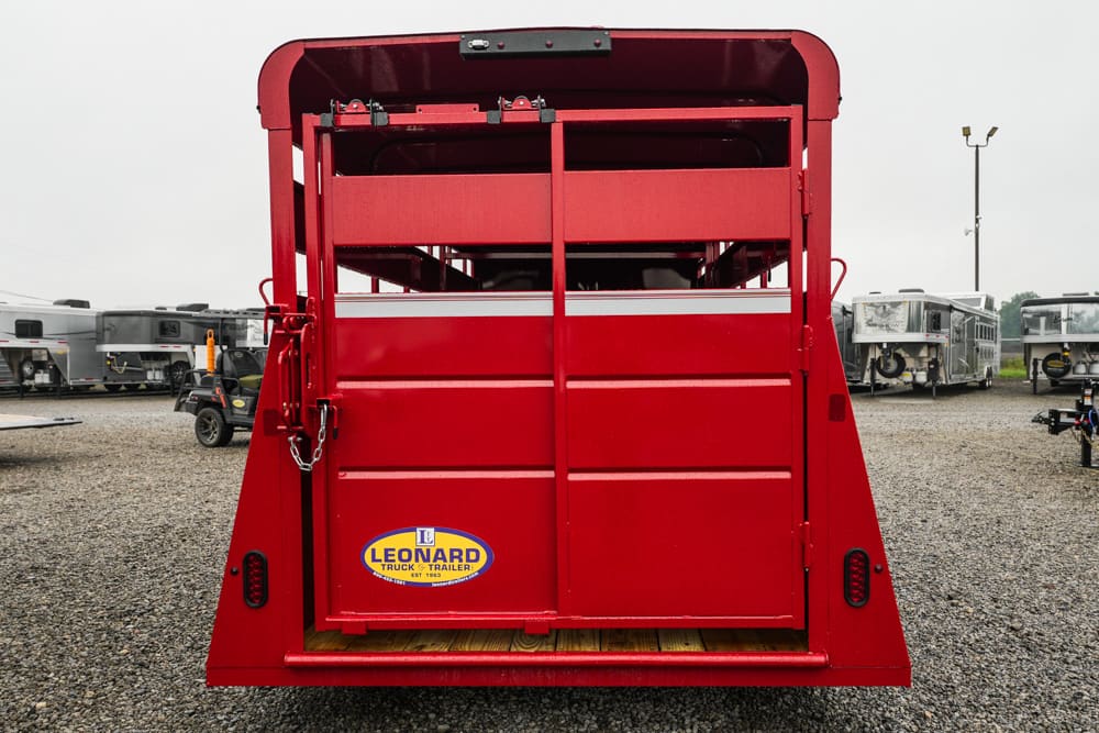 Rear view of a red livestock trailer with its rear gate raised, Leonard Truck & Trailer logo visible on the lower left side on a gravel lot.