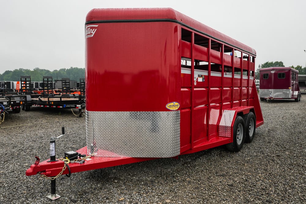 Red livestock trailer with tandem axles and diamond-plate front parked on a gravel lot. Route to transport animals.