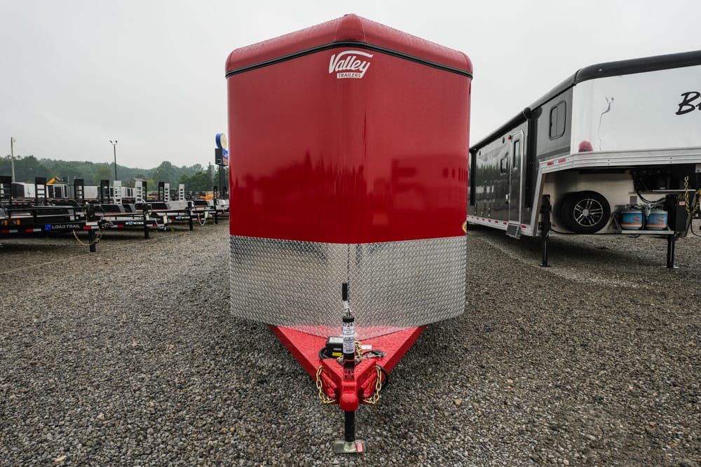 Front view of a red enclosed cargo trailer with a silver diamond-plate lower front, hitch and jack visible on a gravel lot; Valley Trailers logo shows at the top edge.
