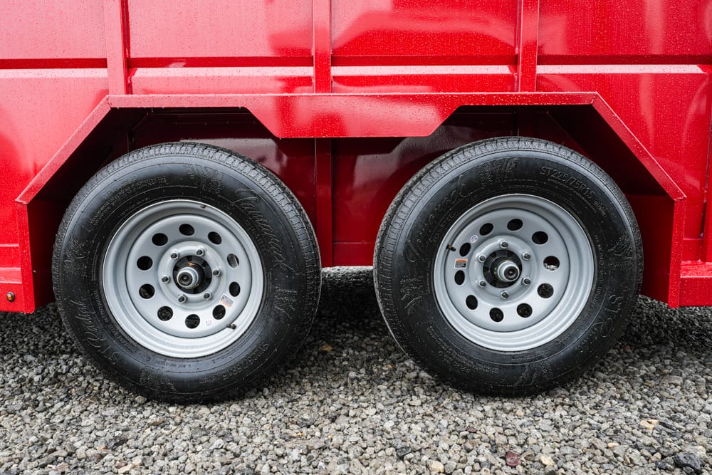 Red trailer with dual-axle wheels on a gravel surface, showing silver steel rims and black tires.