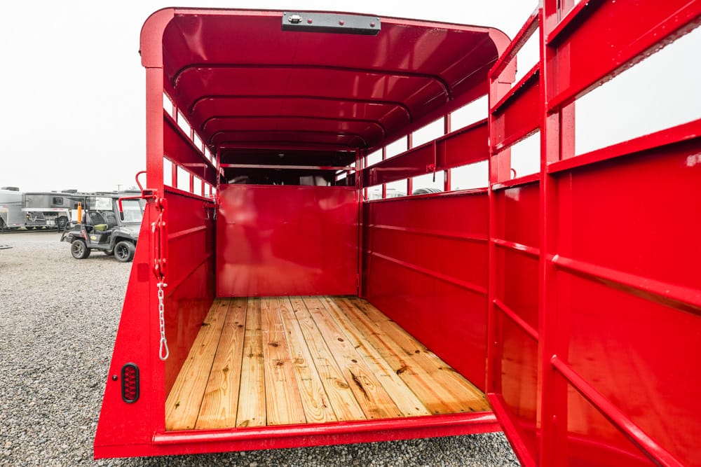 Open red trailer bed with wooden floor, viewed from the back on a gravel lot