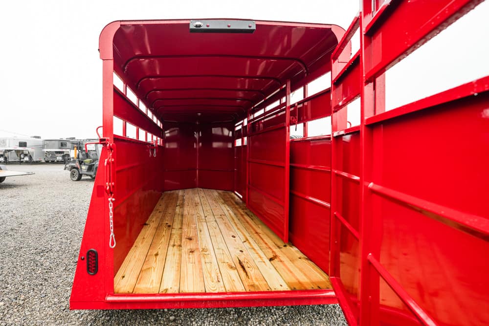 Interior of a bright red trailer with a wooden plank floor and open rear, parked on gravel.