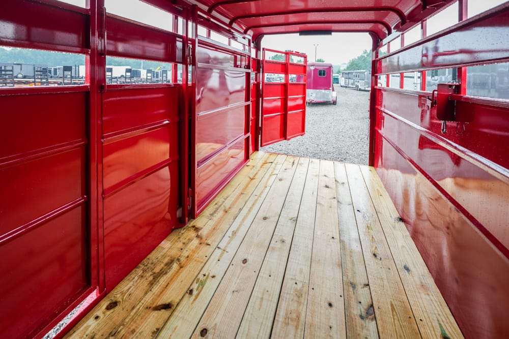 Inside a red trailer with a wooden floor, open back doors, and other trailers visible in a gravel lot outside