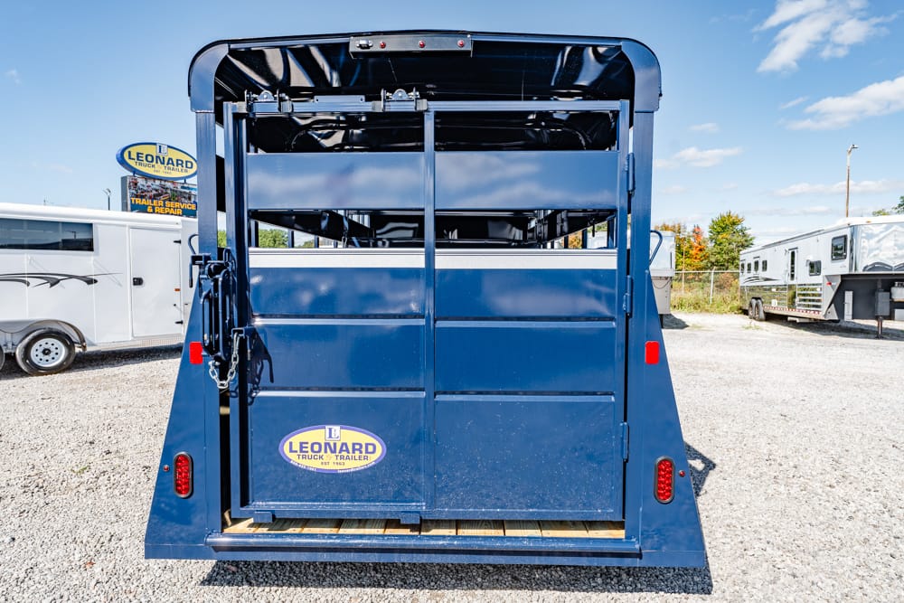 Rear view of a blue Leonard-brand truck trailer on a gravel lot, with closed gates and a wooden ramp at the bottom.