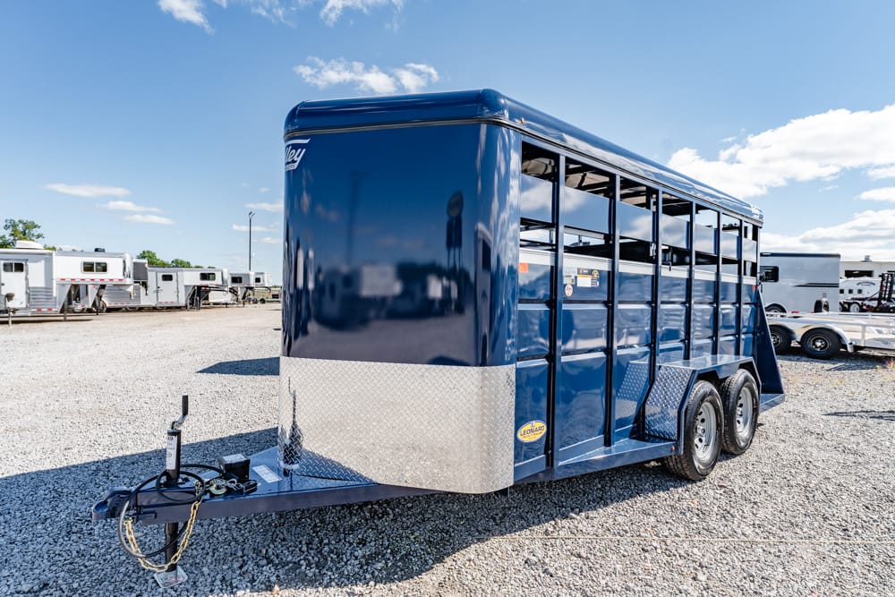 Blue livestock trailer with diamond-plate front, parked on a gravel lot.