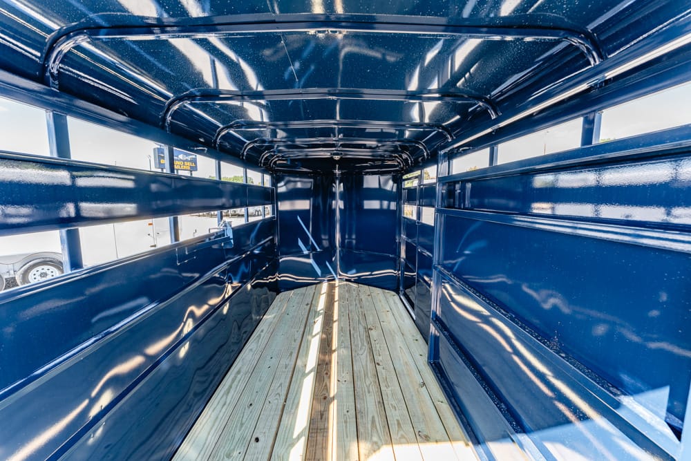 Interior of a blue metal cargo trailer with a wooden plank floor, empty and sunlit with reflections on the walls.