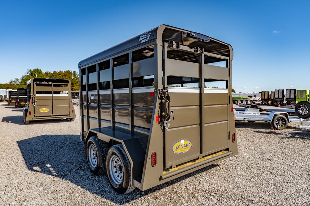 Olive green two‑axle livestock trailer with rear doors and Leonard logo in a gravel lot.