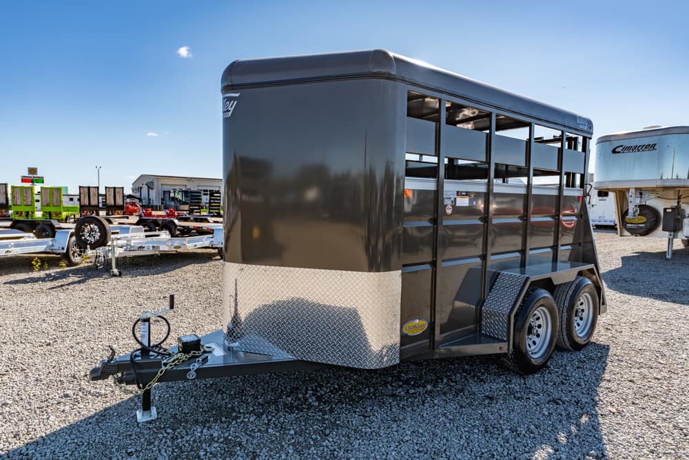 Black livestock trailer with a diamond-plate front, two axles, and side ventilation slats on a gravel lot.