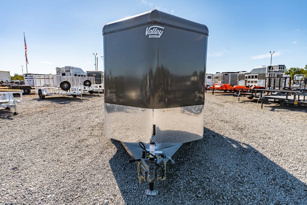 Front view of a black enclosed cargo trailer with chrome diamond-plate lower front, hitch and Valley Trailers logo, in a gravel lot with other trailers nearby.