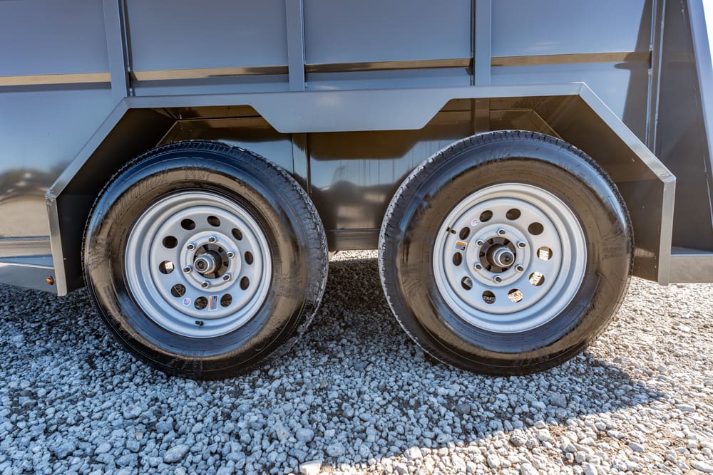Dual trailer wheels with steel rims on a gravel surface under a gray trailer body