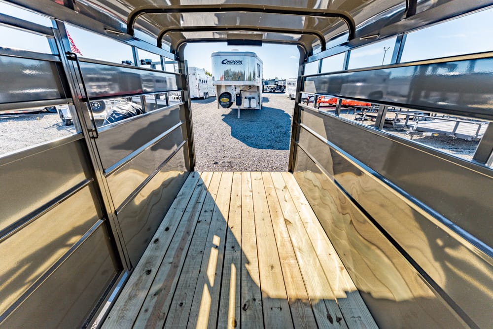 Interior of an empty aluminum trailer with a wooden floor, looking out toward a travel trailer in a dealership RV yard on gravel.