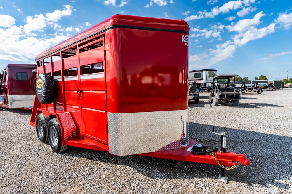 Red livestock trailer with diamond plate front parked on gravel lot, attached to a hitch and spare tire mounted on side edge