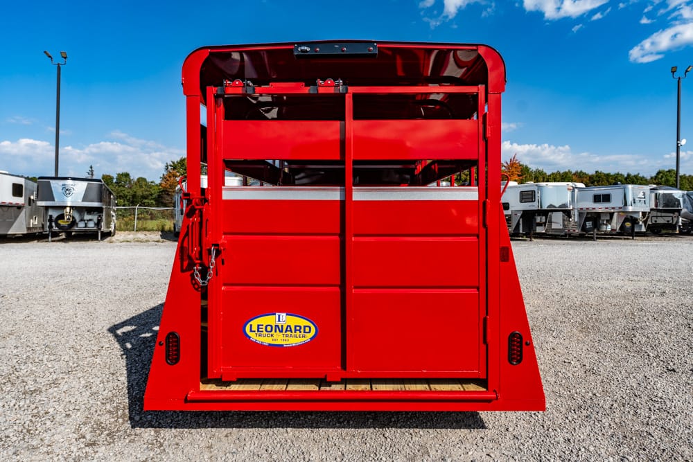Rear view of a bright red trailer with closed doors and a Leonard Truck & Trailer sticker on gravel, blue sky above.